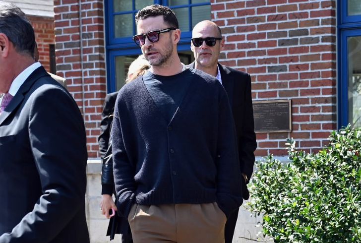 Justin Timberlake look with a black crewneck beneath a black V-neck cardigan, paired with brown trousers